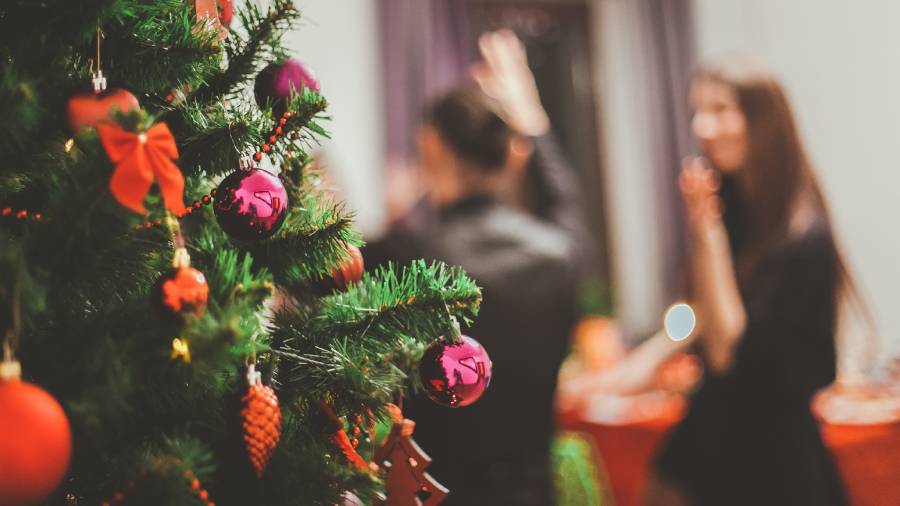 A decorated Christmas tree with ornaments in the foreground, with blurred figures of people from the Human Resources team conversing in the background at a holiday gathering.