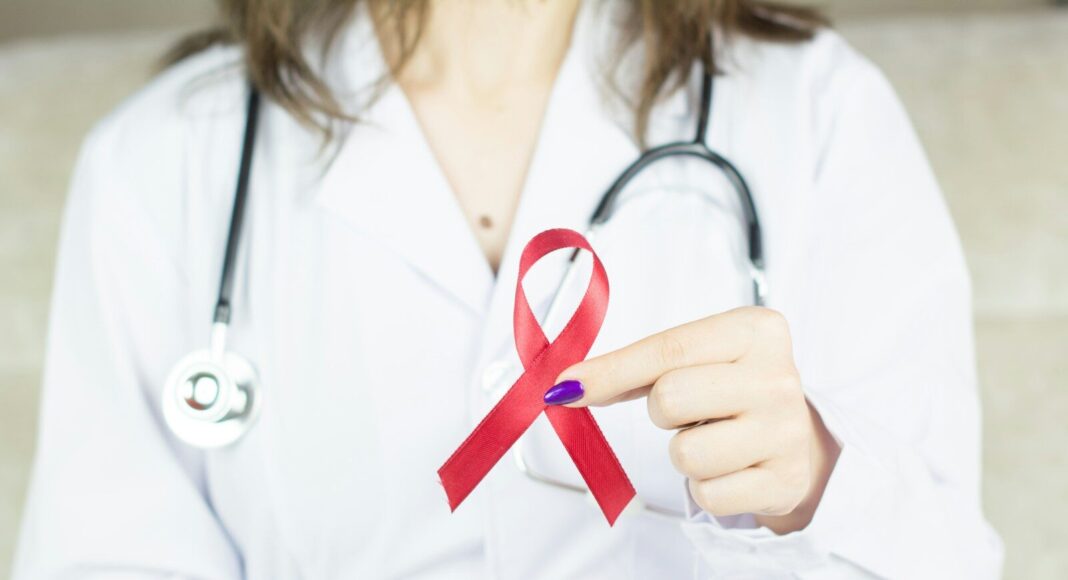 A doctor wearing holding a red cancer ribbon.