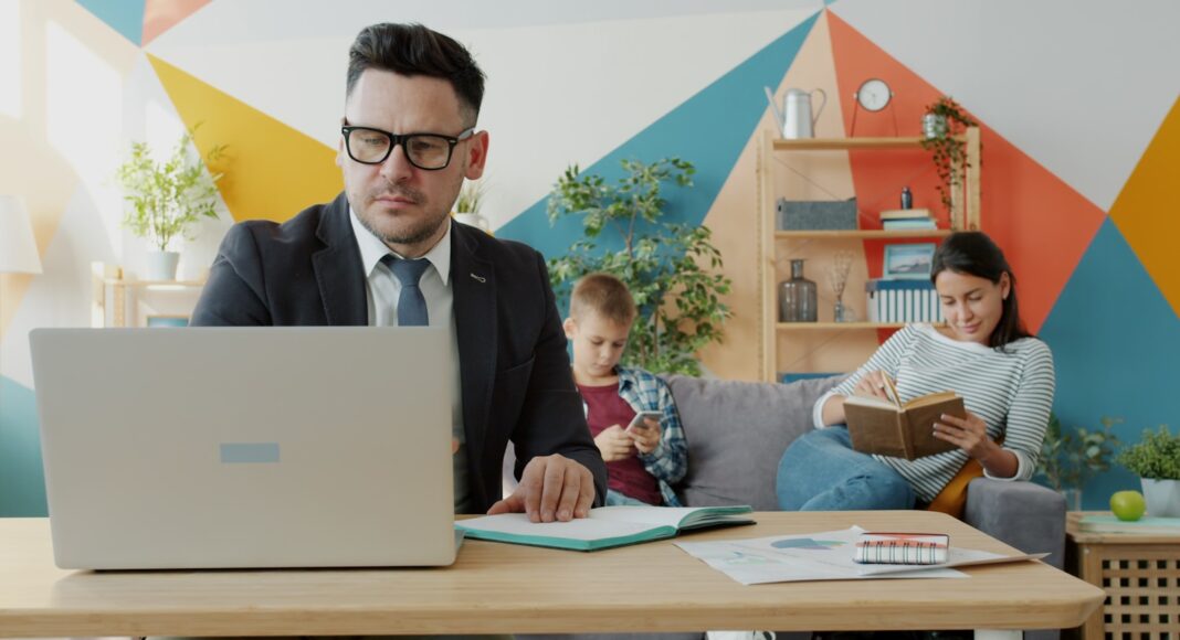 A man working on a laptop while family relaxes in background