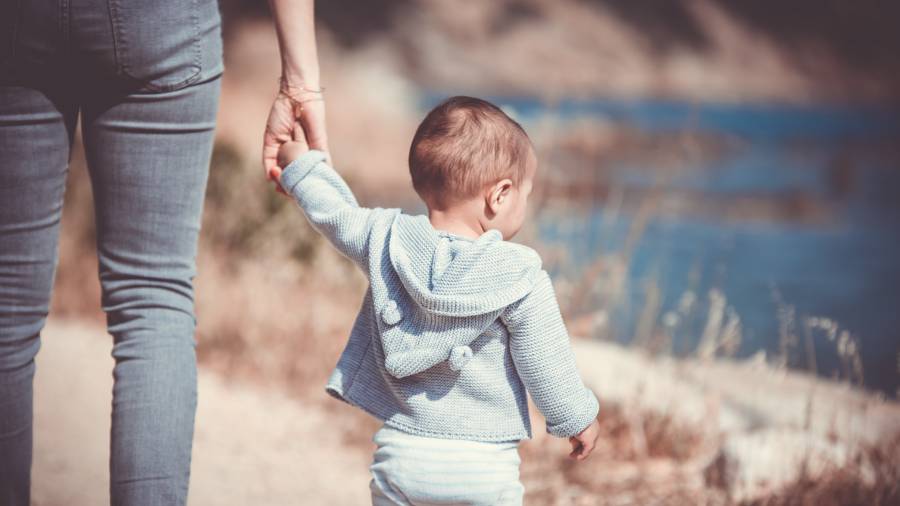 An adult holding the hand of a baby wearing a blue hoodie, walking along a path by the water—a perfect reminder of the essence of people management.