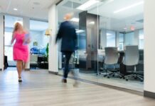 Business groups warn guaranteed hours plans risk fewer jobs and reduced hiring A blurry photo of a man and a woman walking in an office.