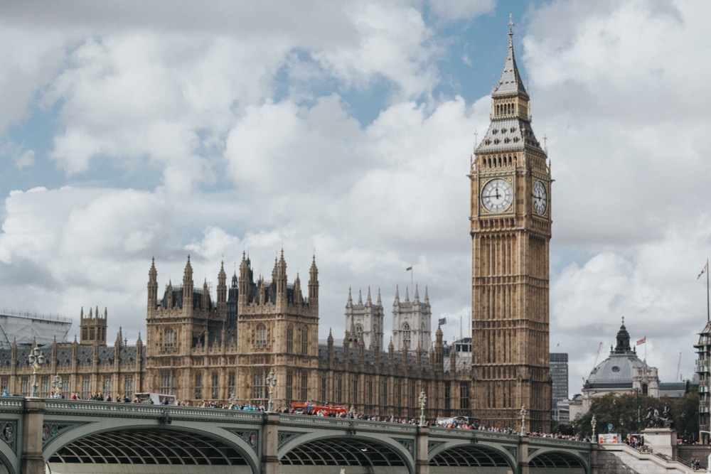 View of the Palace of Westminster and Big Ben in London, with Westminster Bridge in the foreground and a cloudy sky in the background—a symbol of British heritage standing tall as discussions on national minimum wage continue within its historic halls.