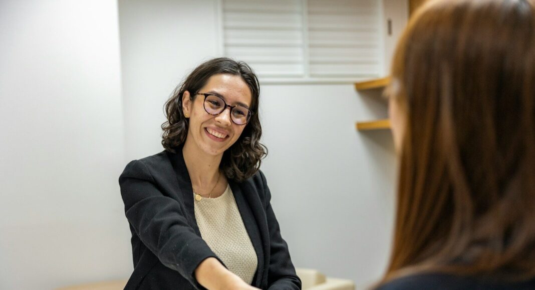 A woman shaking hands with another woman sitting at a table.