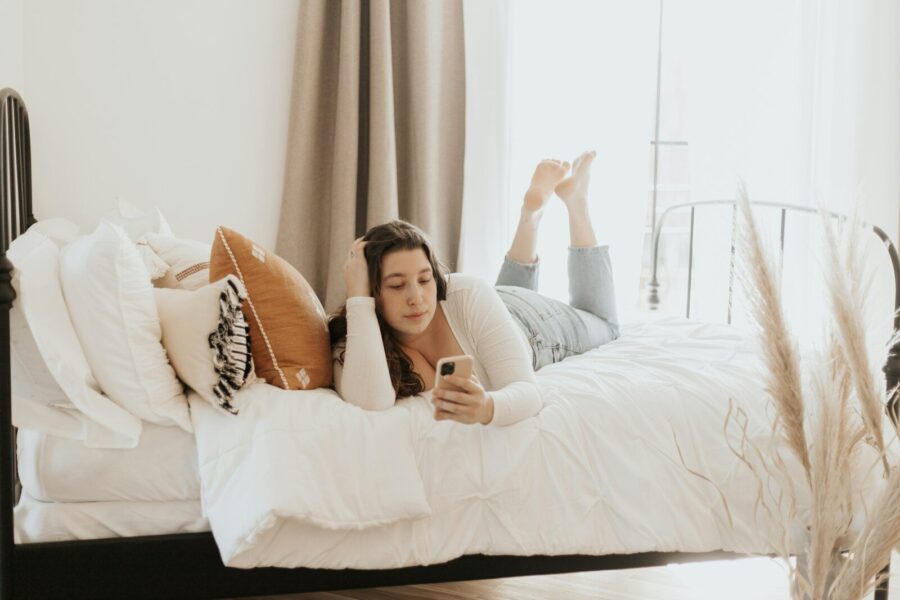 A woman lying on a bed while on her phone.