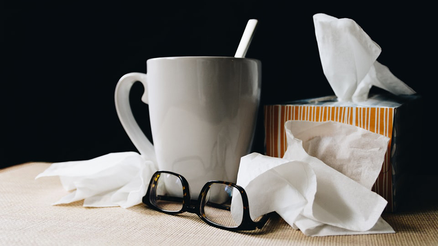 A white mug with a spoon, a box of tissues, scattered tissues, and a pair of glasses on an HR manager's desk.