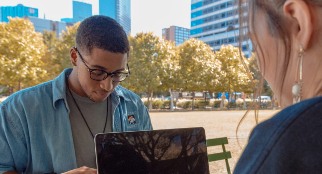 A young man and woman working on laptops outside.