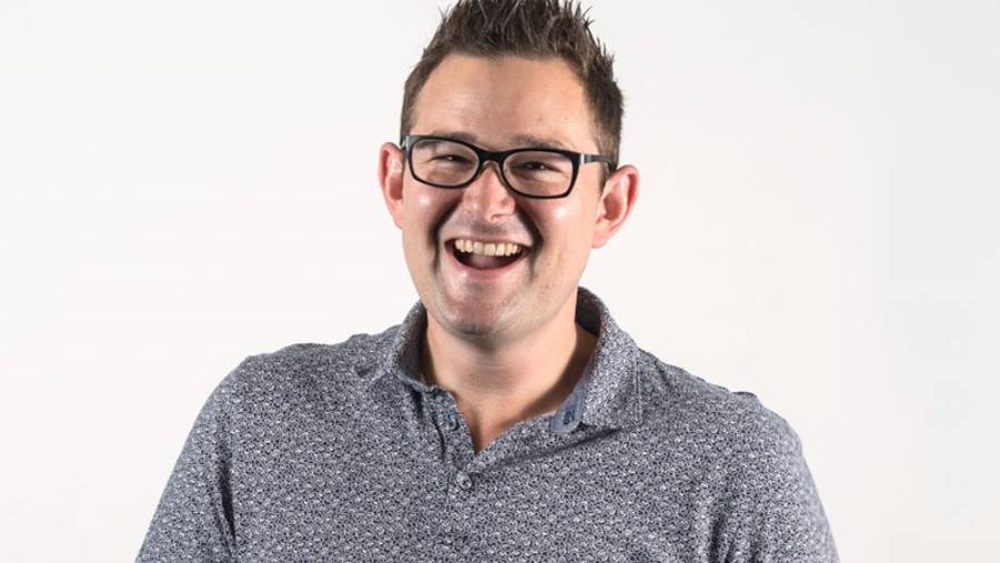 A man with short hair and glasses, wearing a patterned polo shirt, smiles broadly against a plain white background, embodying the approachable essence of people management.