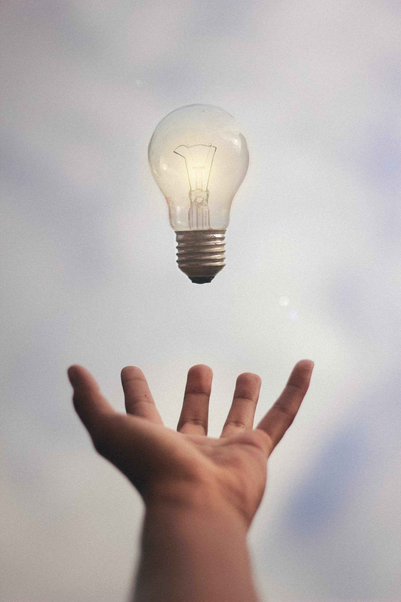 A hand is reaching out towards a light bulb that appears to be floating in the sky, symbolizing the limitless potential of neurodiverse employees.