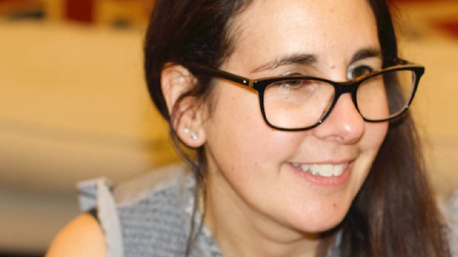 A woman with long dark hair and glasses smiles while looking slightly off-camera. She is wearing a sleeveless top, embodying the approachable and professional vibe often seen in HR personnel.