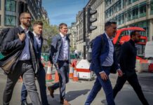 Unemployment falls as private sector pay growth slows to 2.9% Men in suits walking along a city street.