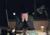 Half of UK workers say their jobs are damaging their health A man in a suit sits at a desk with his head in his hands.