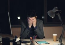 Half of UK workers say their jobs are damaging their health A man in a suit sits at a desk with his head in his hands.