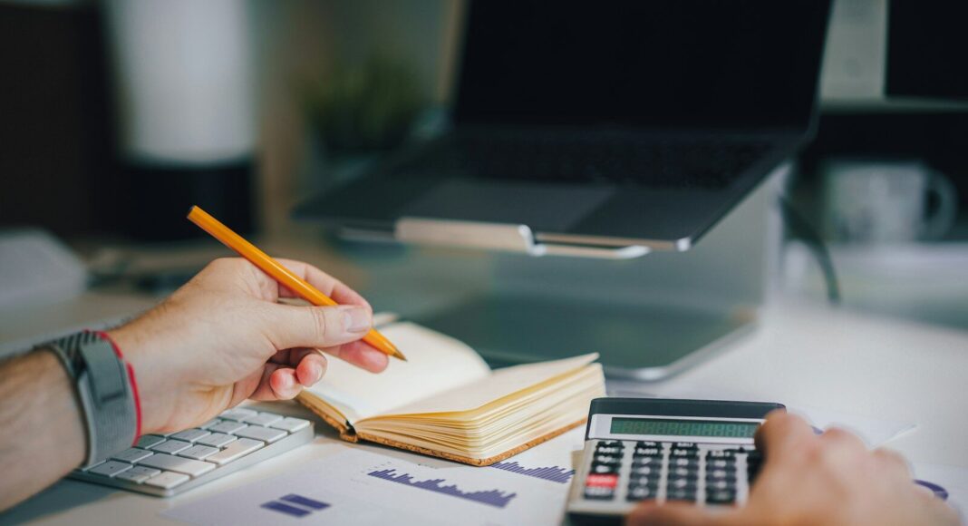 A person doing accounting tasks with a pencil and calculator.