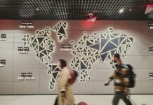 Govt unveils visa support scheme to help scale-ups hire global talent People walk past a glowing world map.