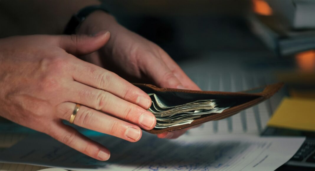 A person putting cash into a wallet.