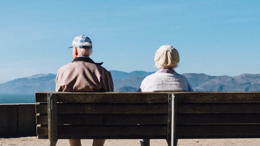 Two older adults sit on a bench facing a scenic view of mountains and clear blue sky, reflecting on years spent in human resources and personnel management.