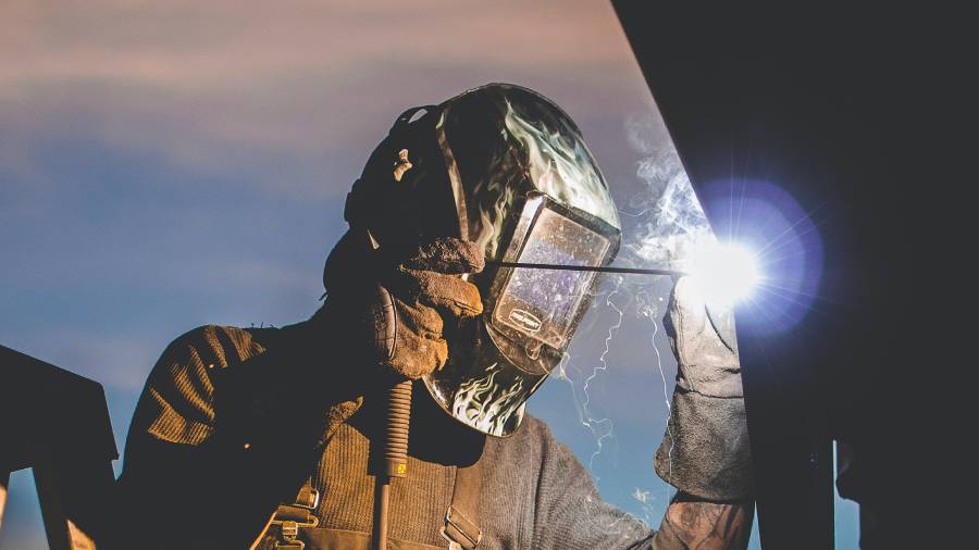 A welder in full protective gear and a helmet deftly uses a welding torch on a metal structure, with sparks flying, illustrating the critical safety standards valued in effective People Management.