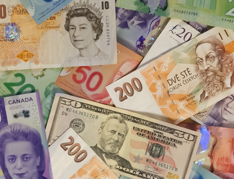 Various currencies, including British pounds, Canadian dollars, Czech koruna, American dollars, and Euro notes are spread out in a pile, symbolizing the foundation of financial wellbeing.