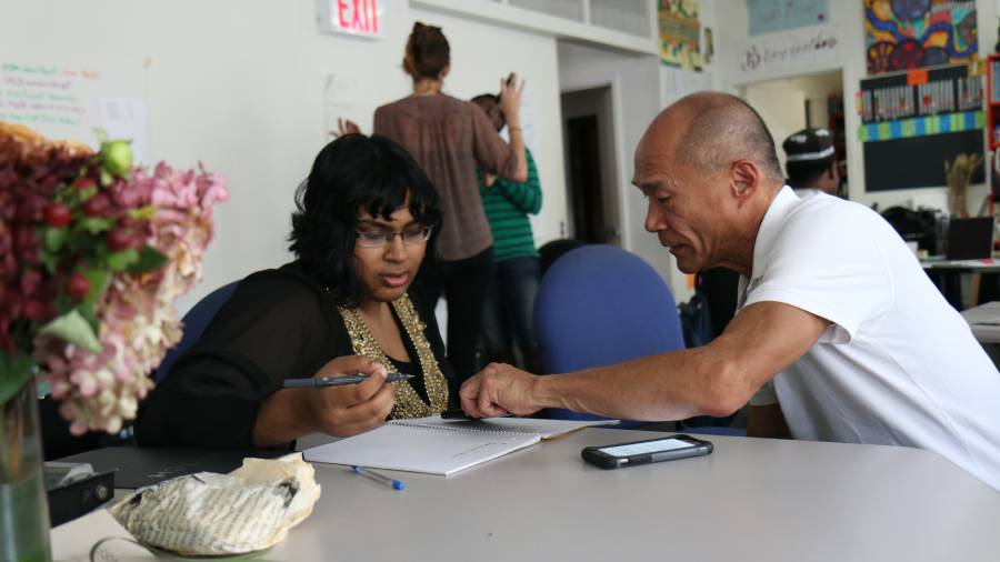 Two people sit at a table, engaged in conversation and looking at documents. One person is holding a pen and pointing at a paper, highlighting the skills shortage, while the other observes. A smartphone and a flower vase are on the table. Two people sit at a table, engaged in conversation and looking at documents. One person is holding a pen and pointing at a paper, highlighting the skills shortage, while the other observes. A smartphone and a flower vase are on the table.