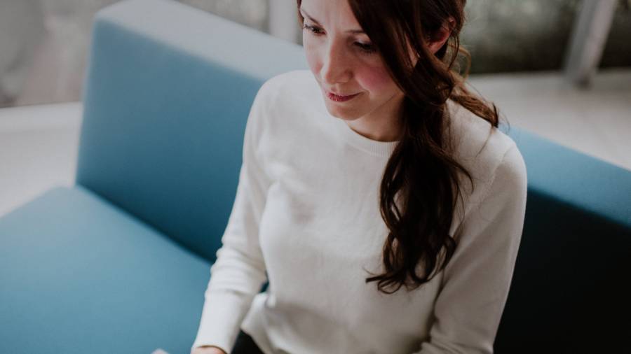 A woman with brown hair wearing a white sweater sits on a blue couch, her thoughts focused on human resources.