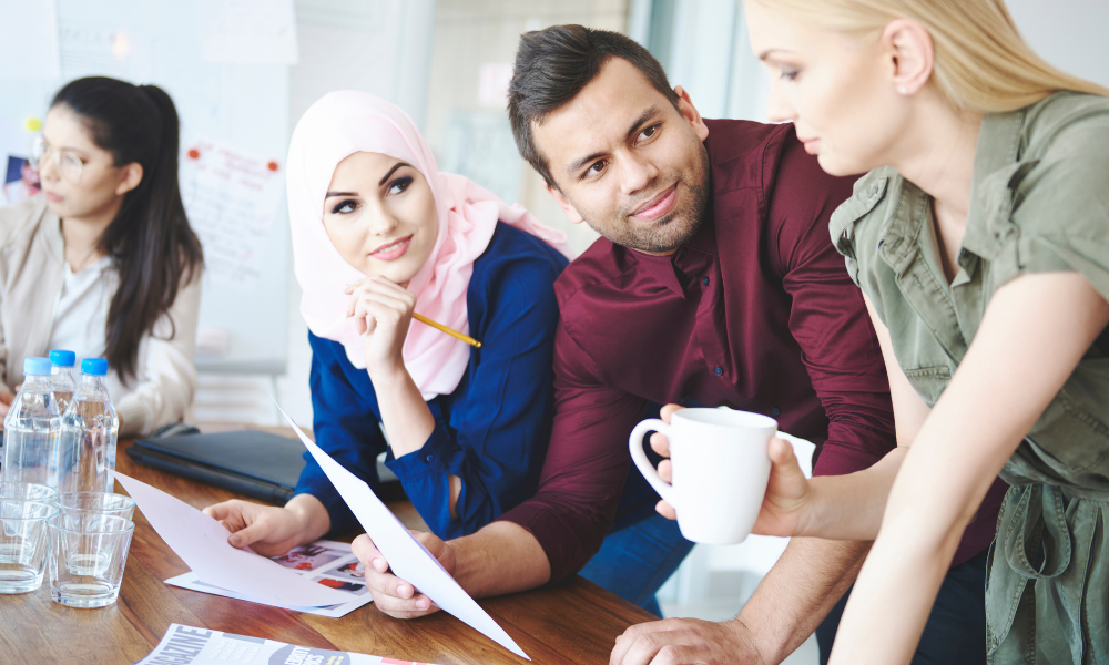 woman in pink hijab talking to a male and female colleague in suits