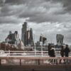 People walking across a bridge in London with a grey, stormy sky in the background.