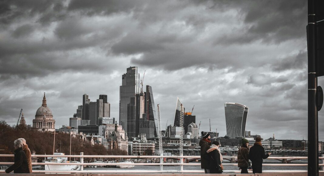 People walking across a bridge in London with a grey, stormy sky in the background.