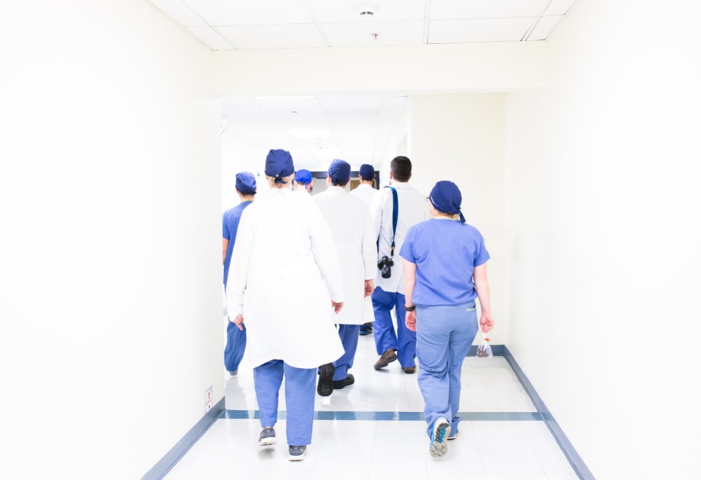 A group of medical professionals in scrubs and lab coats walks down a well-lit hospital hallway, dedicated to addressing BME inequalities in healthcare.
