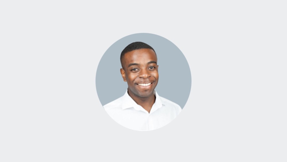 A person smiling, wearing a white collared shirt, and set against a light gray background, embodies the spirit of racial equity through their confident and inclusive demeanor.