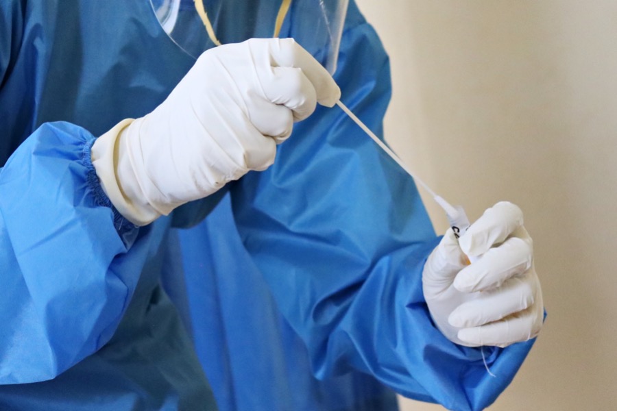 A person wearing blue protective gear and gloves prepares a swab sample for testing amid the pandemic.