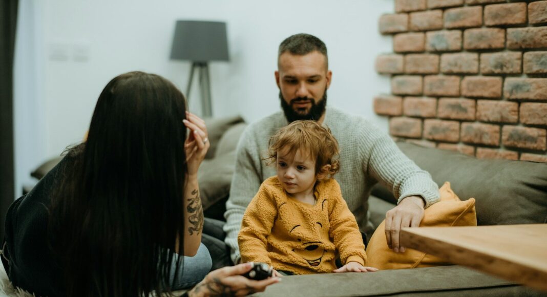 A man and woman sit on a sofa with their small child.