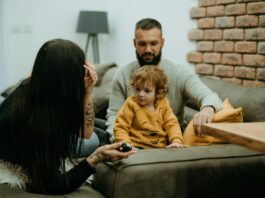 Employers must do more to support family life for millennials, Gen Z and Gen Alpha A man and woman sit on a sofa with their small child.