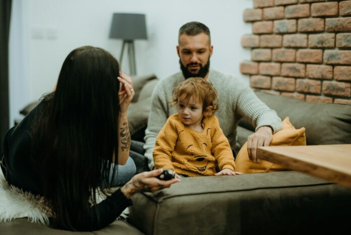 Photo by Tamara Govedarovic A man and woman sit on a sofa with their small child.