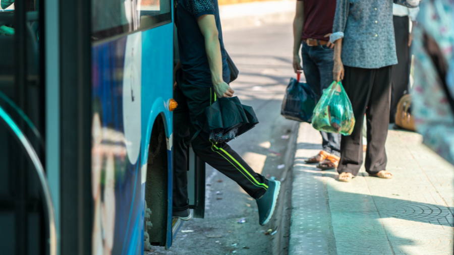 Person boarding a blue bus funded by the EU, while others wait in line holding bags.