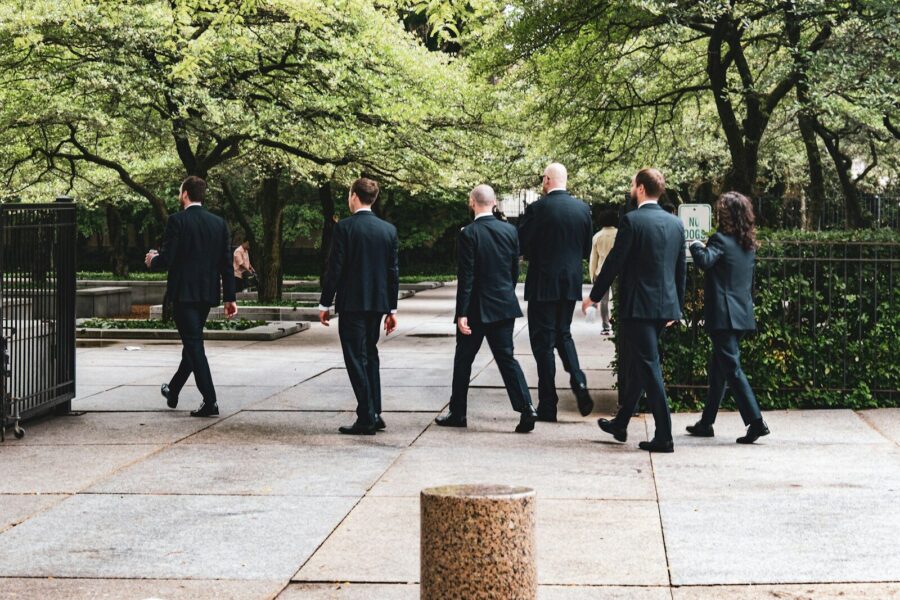 Men and women in suits, walking by a park.