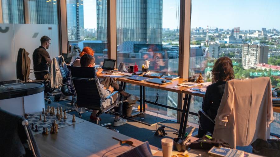 A modern office with several HR personnel working at desks in front of large windows overlooking a cityscape.