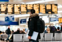 Employers face growing duty of care pressures as business travel costs surge A male passenger stands in front of a departures board at an airport.