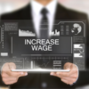 A person in a suit holding a digital tablet displaying the text "Increase Wage" is surrounded by various data charts and graphs highlighting wages and inflation.