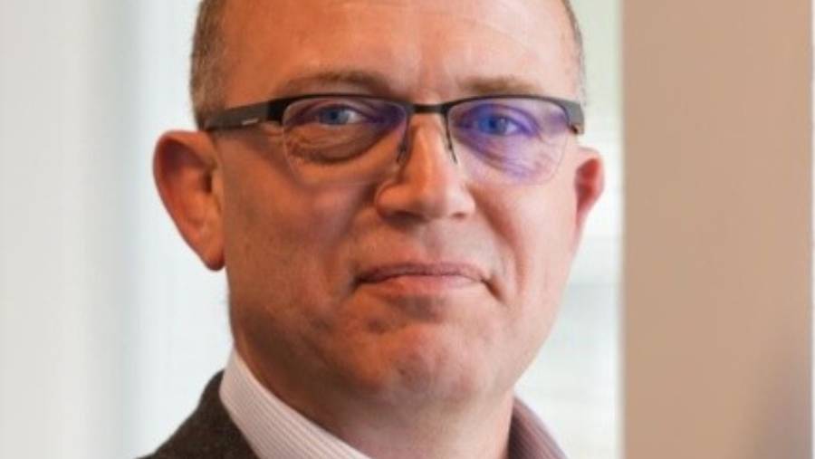 A middle-aged man with short hair and glasses, wearing a suit and a light-colored shirt, looks at the camera, embodying the professionalism often seen in Human Resources.