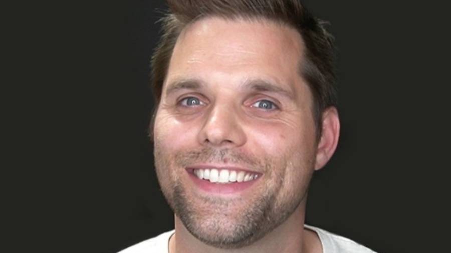 A man with short brown hair and a beard, specializing in people management, smiles at the camera against a plain, dark background.