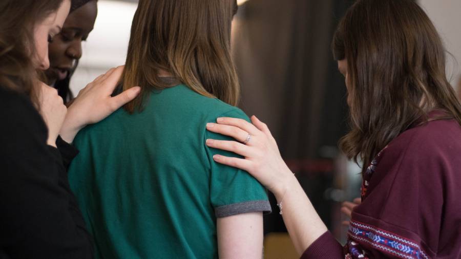 Four individuals with their hands on each other's shoulders in a supportive manner, seen from the back, symbolizing the unity and strength promoted by the Miscarriage Association.