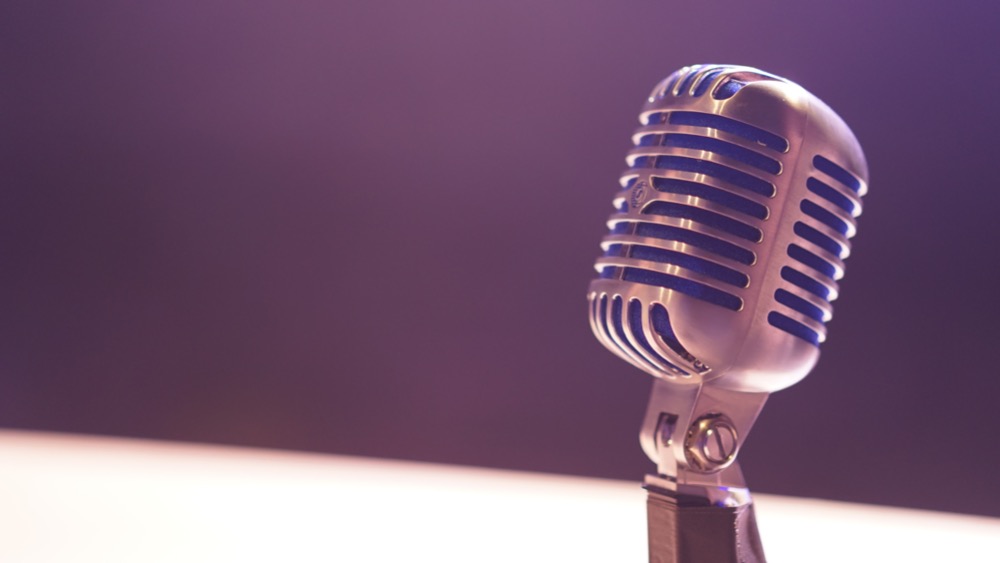 A silver vintage-style microphone with blue accents is displayed against a purple background, evoking a sense of nostalgia while highlighting the importance of clear communication in regional hiring.