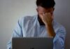 Workers ‘pushing through illness’ as workplace pressure grows A man with his hand to his head while working at a laptop, suggesting illness at work.