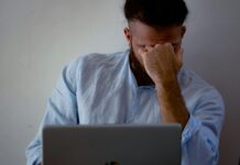 Workers ‘pushing through illness’ as workplace pressure grows A man with his hand to his head while working at a laptop, suggesting illness at work.