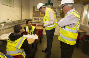 Four construction workers in safety vests and helmets discussing HR documents inside a site office.