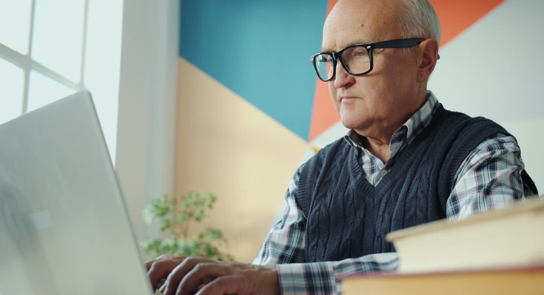 Elderly man with glasses using a laptop.