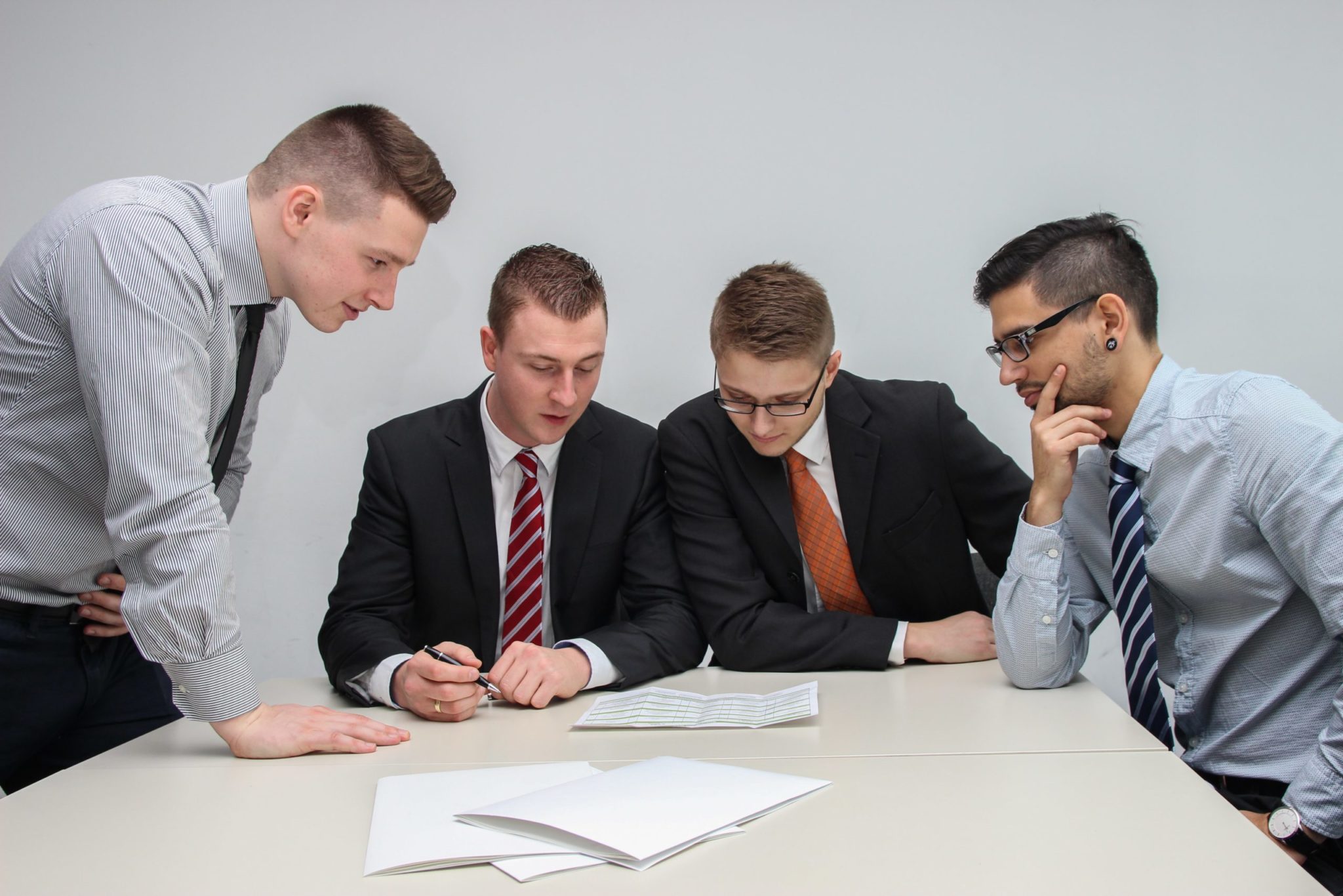 Four men in business attire are gathered around a table, closely examining HR documents.