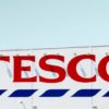 A large sign with the red letters "TESCO" and blue stripes below, mounted on the side of a white building, visible from the HR department windows.