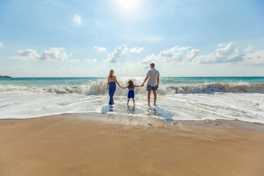 A man, woman and child holding hands at the seashore.