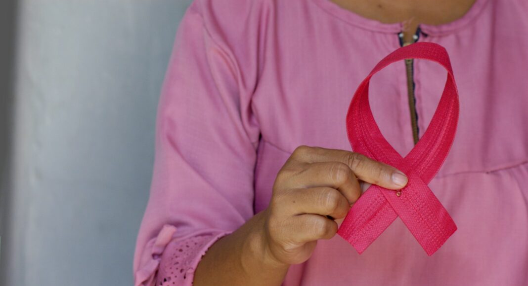 A woman in pink holding a pink cancer ribbon.